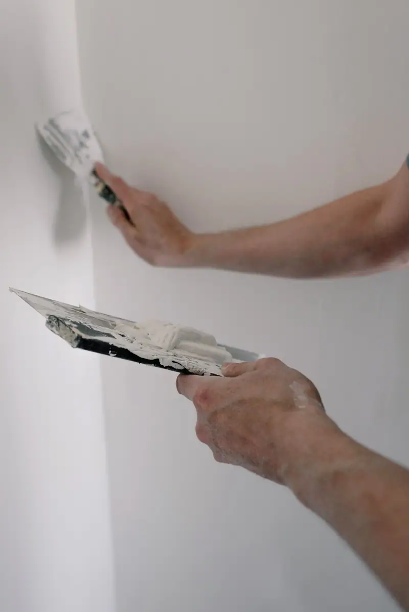 Two hands working joint compound into an inside corner with drywall knives