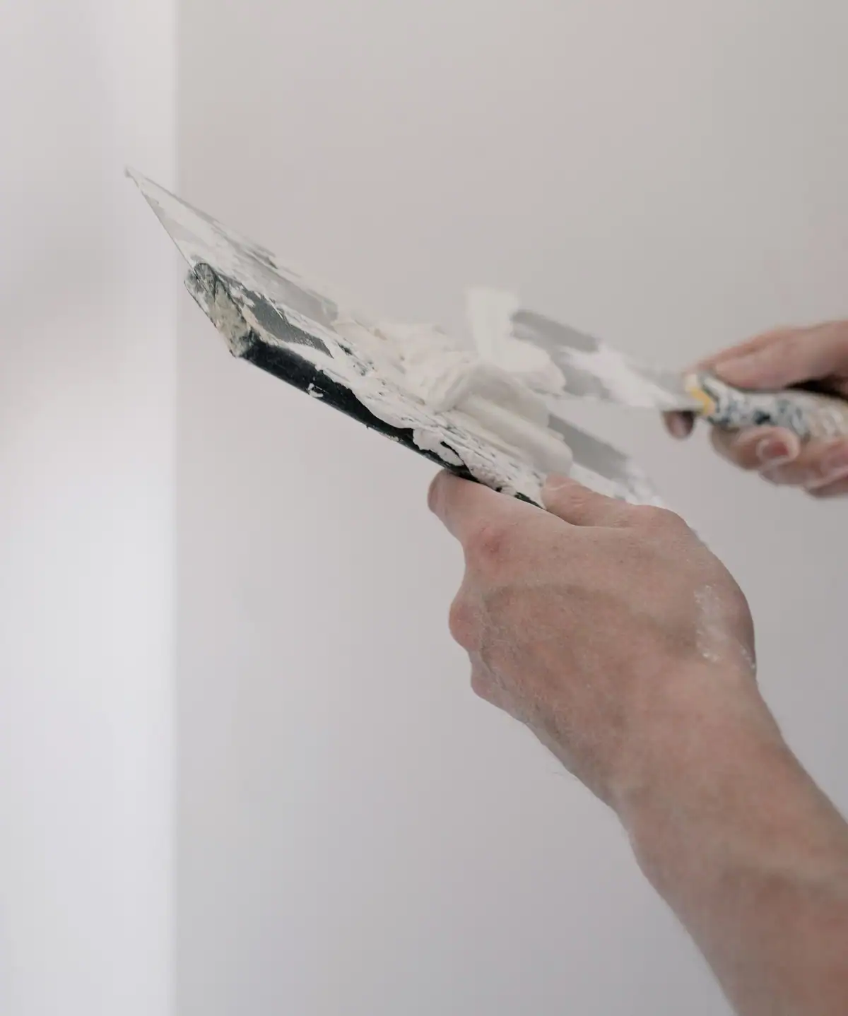 Hands loading joint compound from a wide knife onto a putty knife