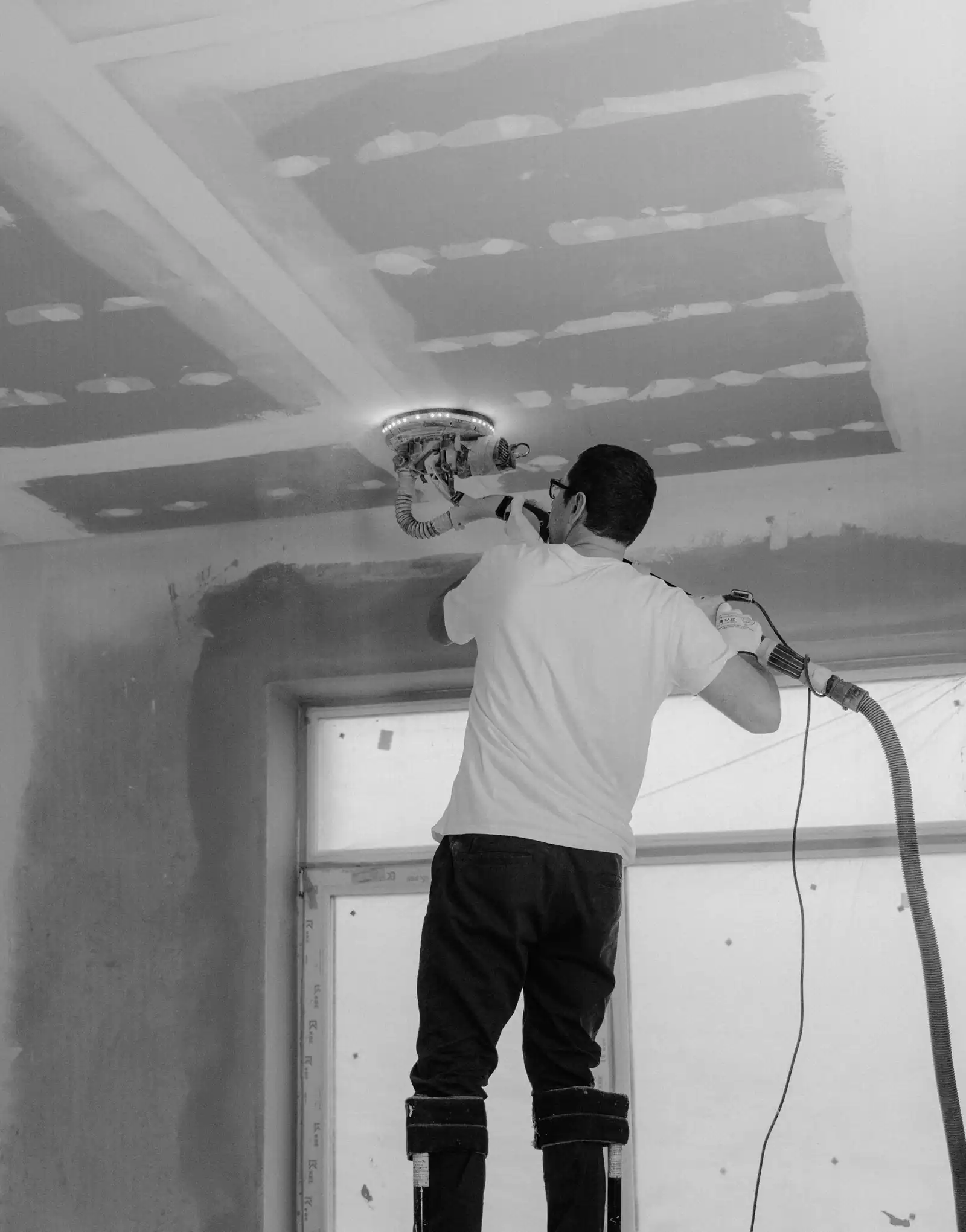Finisher on stilts sanding a taped drywall ceiling