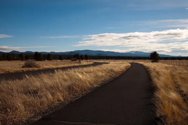 Paved bike path through meadow grass toward pines and buttes in Sunriver, Oregon